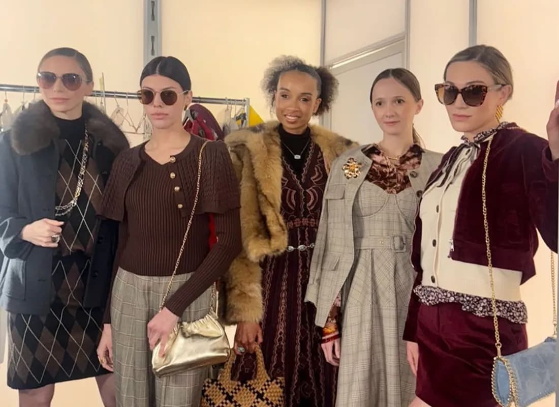Three models backstage in autumnal knitwear, a shearling vest and a tailored pinafore